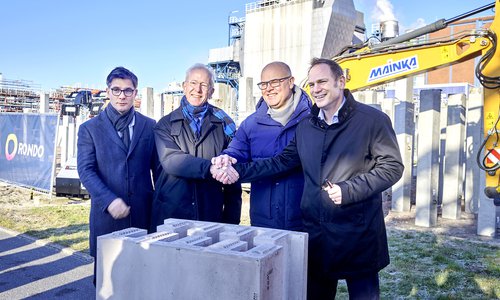 Vier Männer beim Handschlag auf einer Baustelle mit Baggern