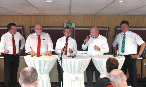 Fünf Männer stehen an Stehtischen und sprechen bei einer Veranstaltung