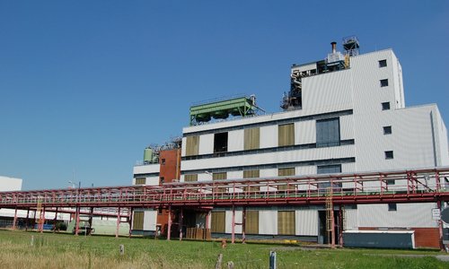 Weißes Fabrikgebäude mit Rohrbrücke auf dem Werksgelände