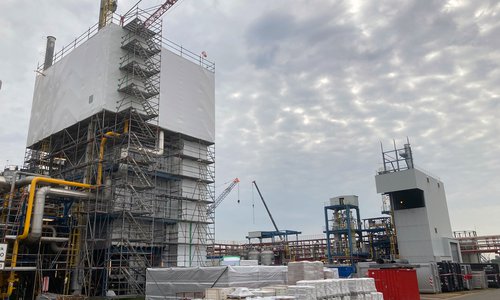 Baustelle mit eingerüstetem Reformerturm und Kran auf einem Werksgelände