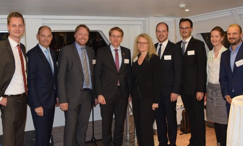 Gruppenfoto von neun Personen in Anzügen an Bord eines Schiffes