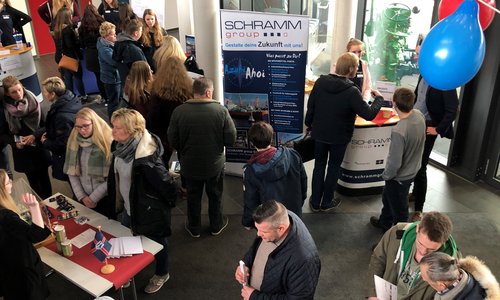 Besucher an Informationsständen einer Ausbildungsmesse mit Luftballons in der Eingangshalle
