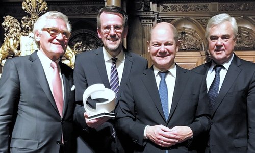 Vier Männer in Anzügen bei einer Preisverleihung, einer hält eine weiße Trophäe