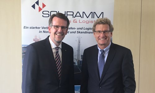 Zwei Männer in Anzügen vor einem Banner von Schramm Ports und Logistics
